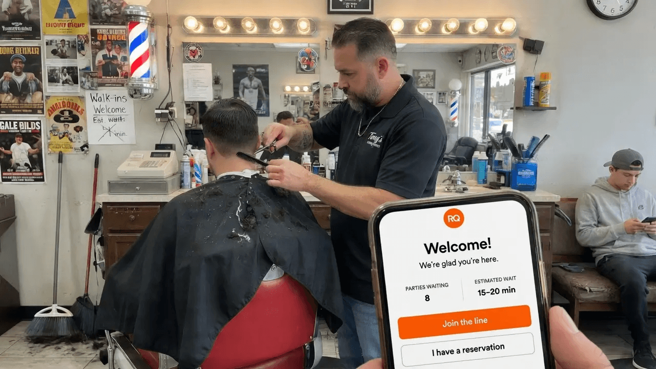 Barber finishing a haircut while the next customer's phone shows they're first in line
